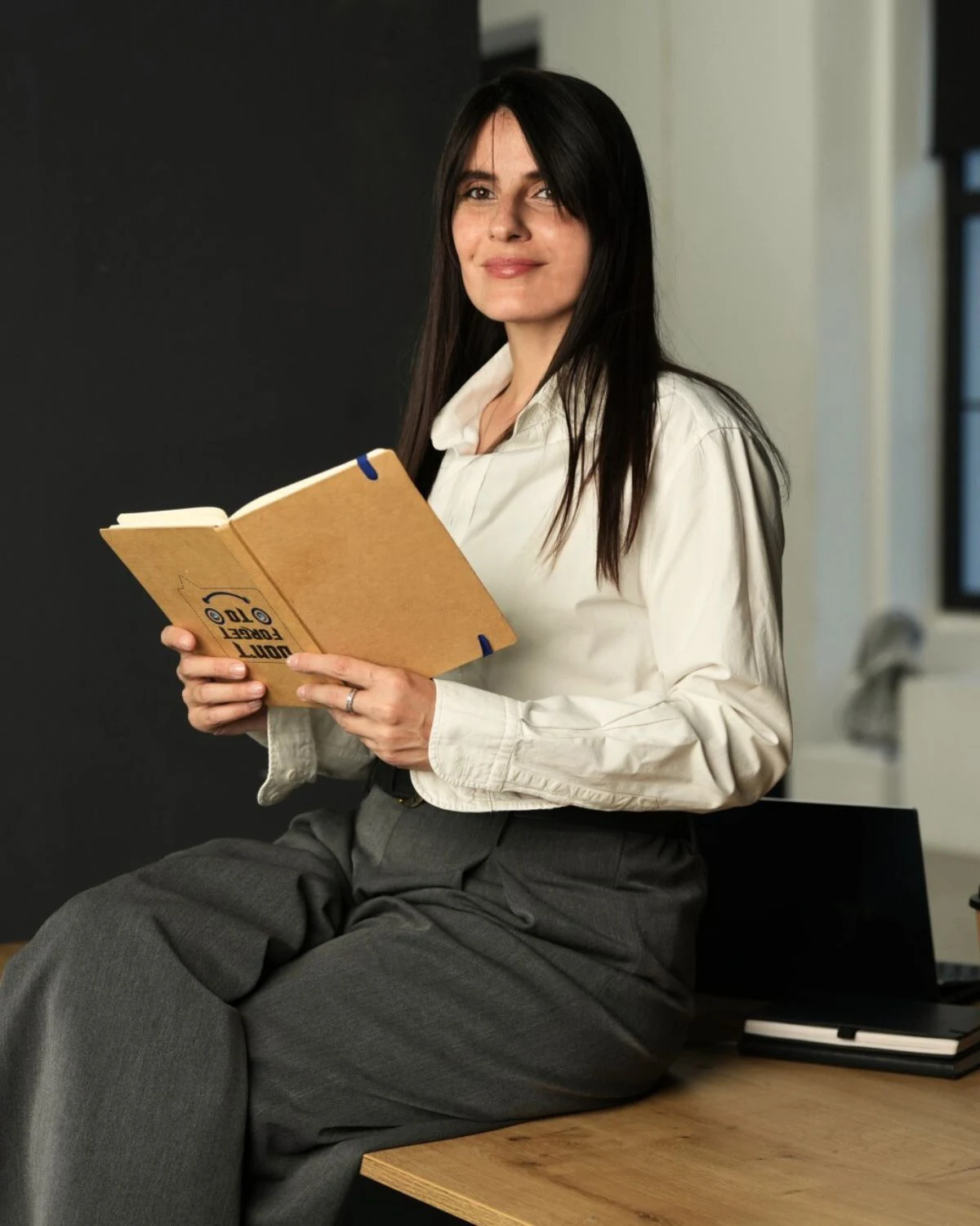 marija sedi na svom radnom stolu prekrstenih nog drzi rokovniku ruci i blago se smeska u kameru