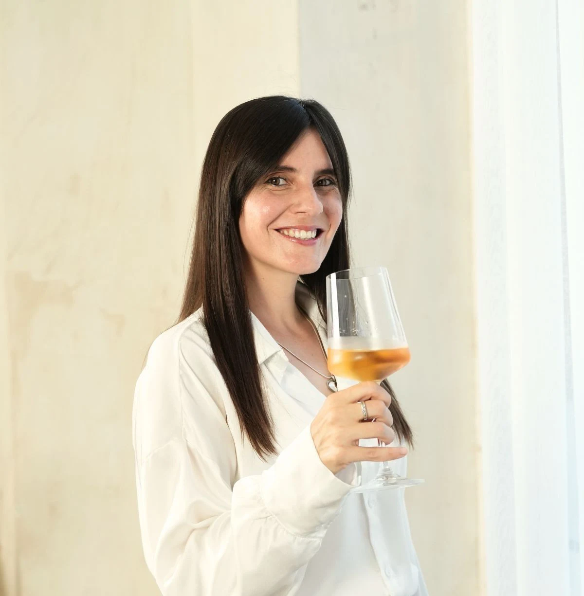 marija stoji uz sirok osmeh i drzi casu belog vina u ruci