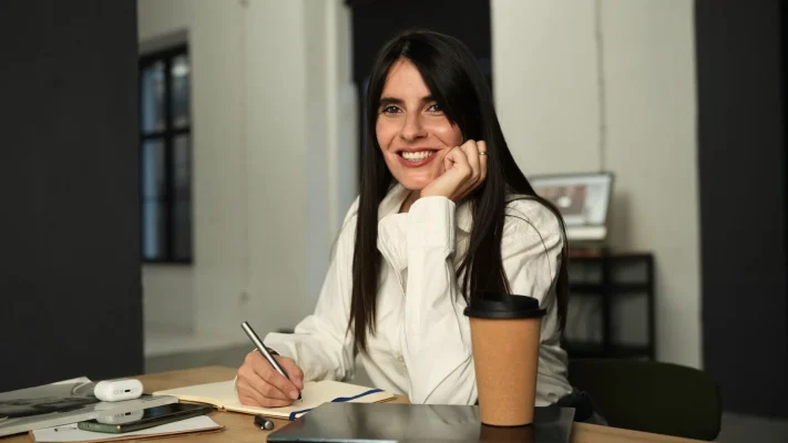 marija sedi u kanceliriji za radnim stolom naslonila je glavu na ruku i smeje se